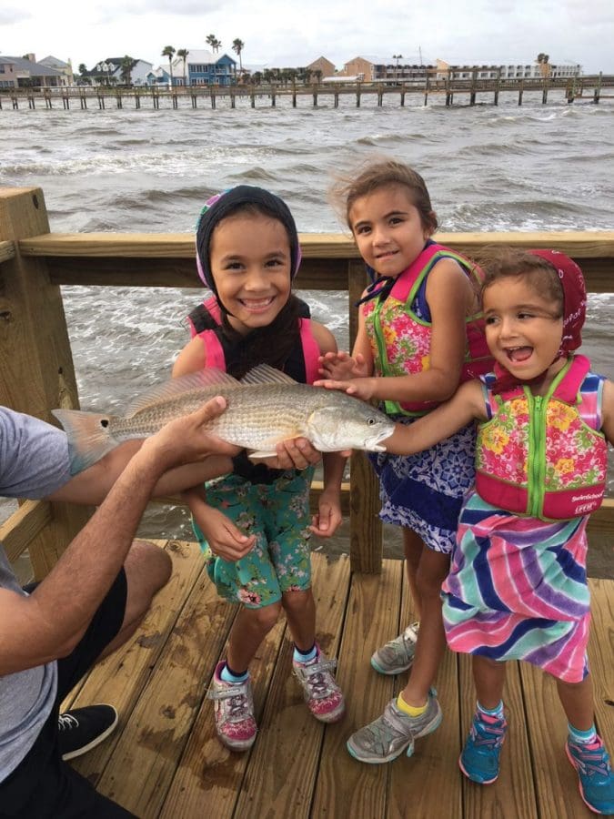 Nine-year-old Isabella Rivera with the biggest fish of her life, 22-inch redfish caught in Aransas Bay on a fishing pier using live shrimp. The fish was released. Joining her were her sisters Abryanna (seven) and Katalyna (four). Dad Mark held the fish.
