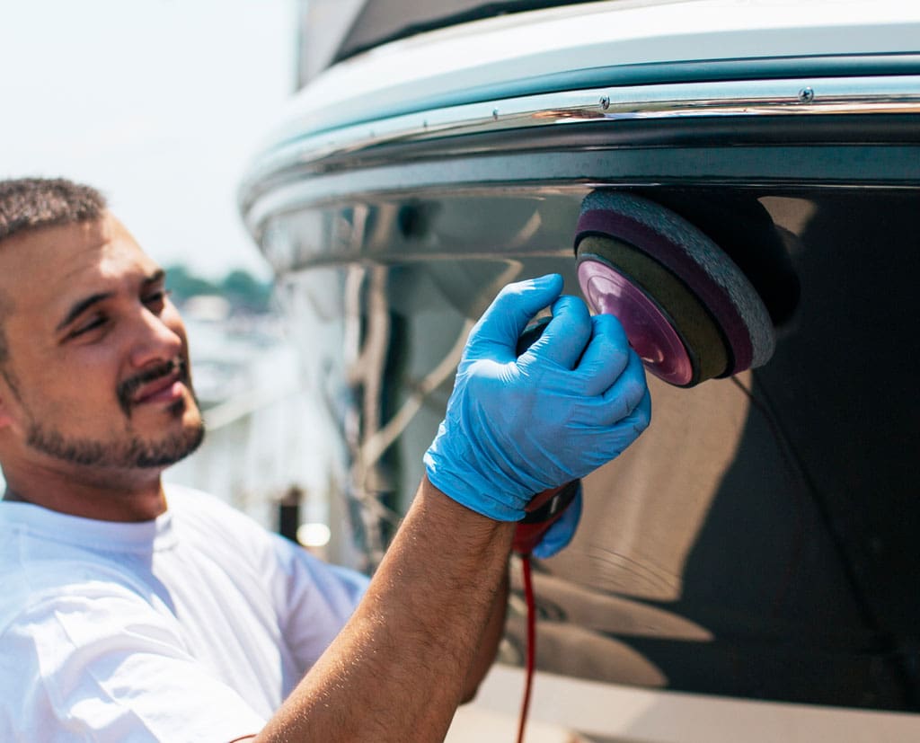 Boat maintenance - Man with orbital polisher polishing boat in marina.